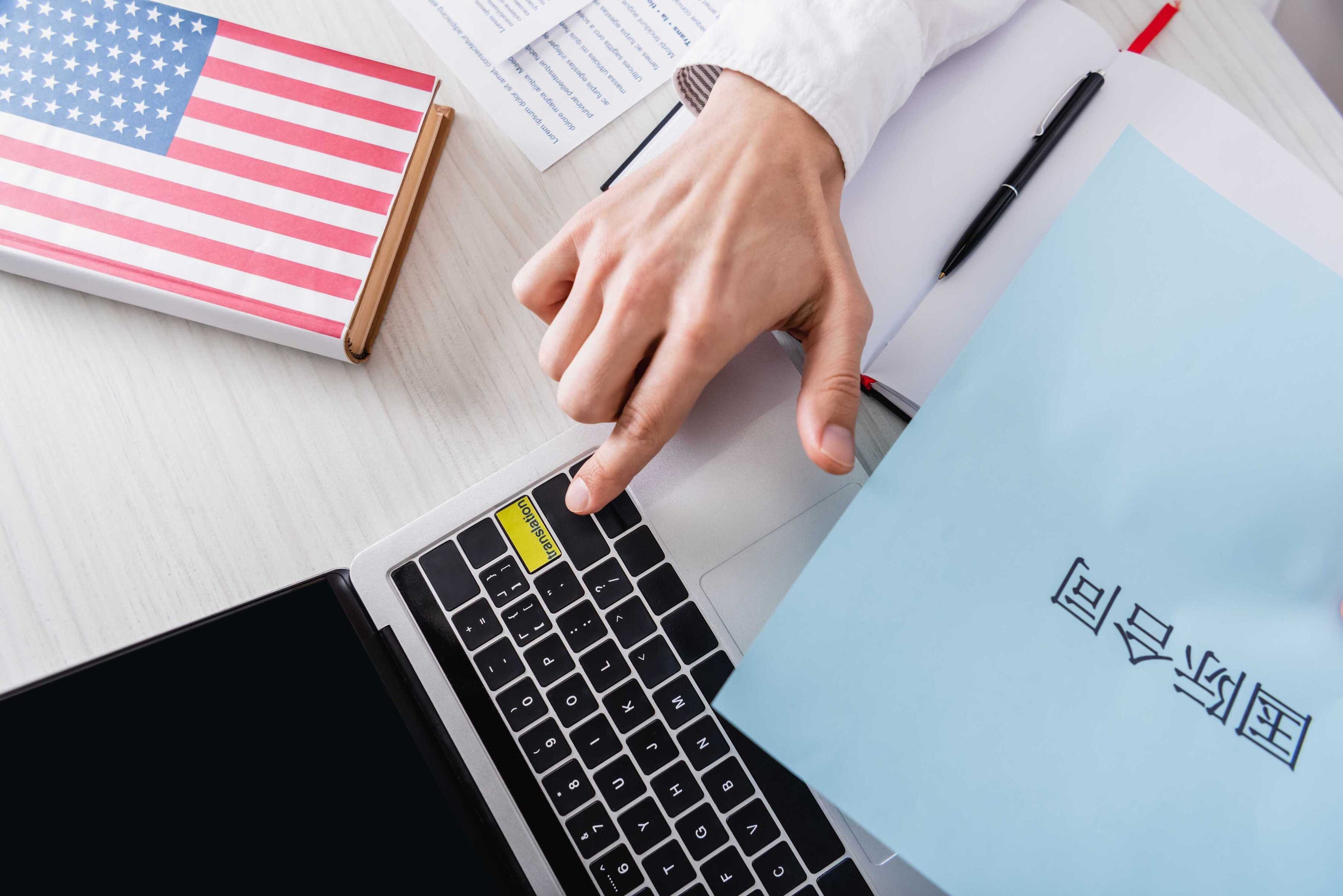 Hand typing on a laptop with an American flag and a document on a desk