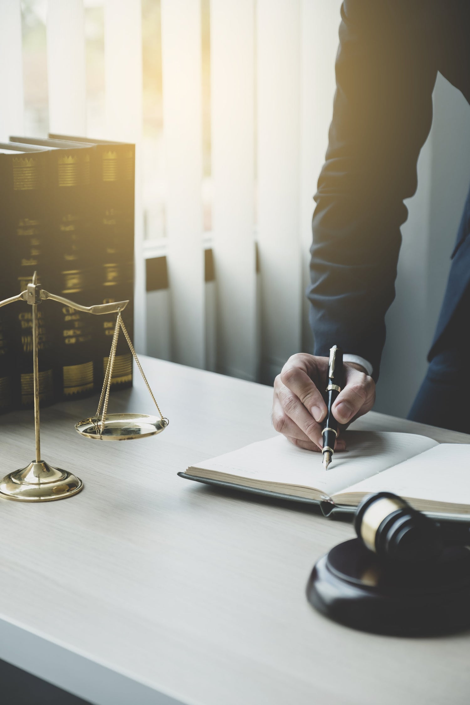 Lawyer writing in a notebook with a gavel and scale of justice on a desk.