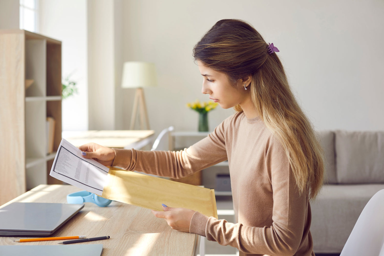 Woman sitting at a table in a bright room, looking at a piece of paper.