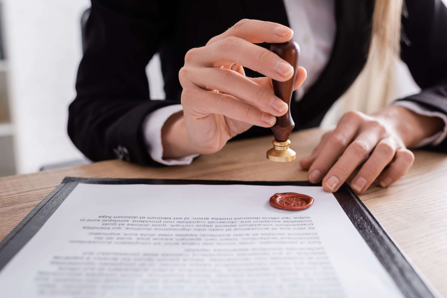 Person sealing a document with a stamp on a wooden desk