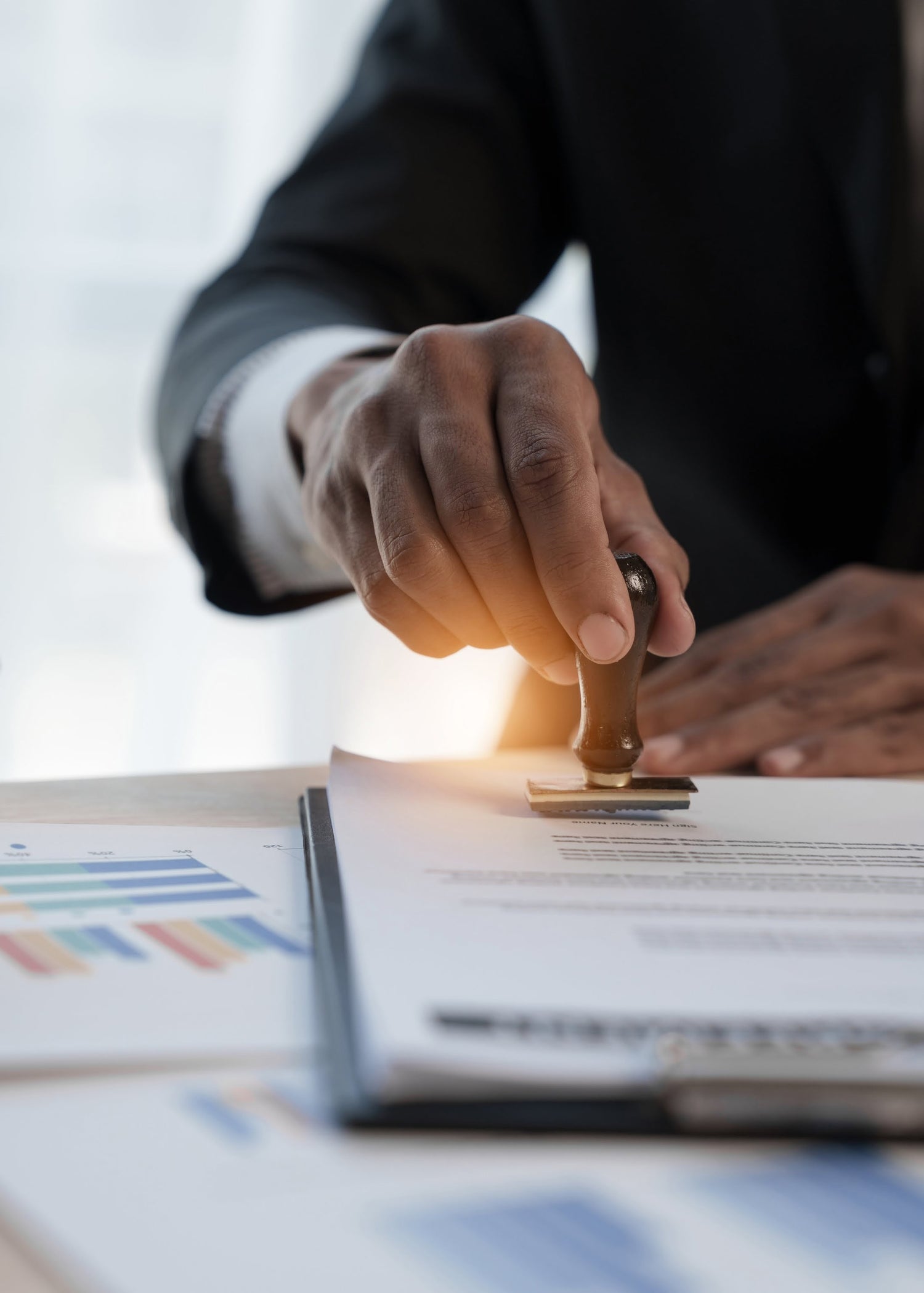 Hand stamping a document with a seal on a desk with graphs in the background
