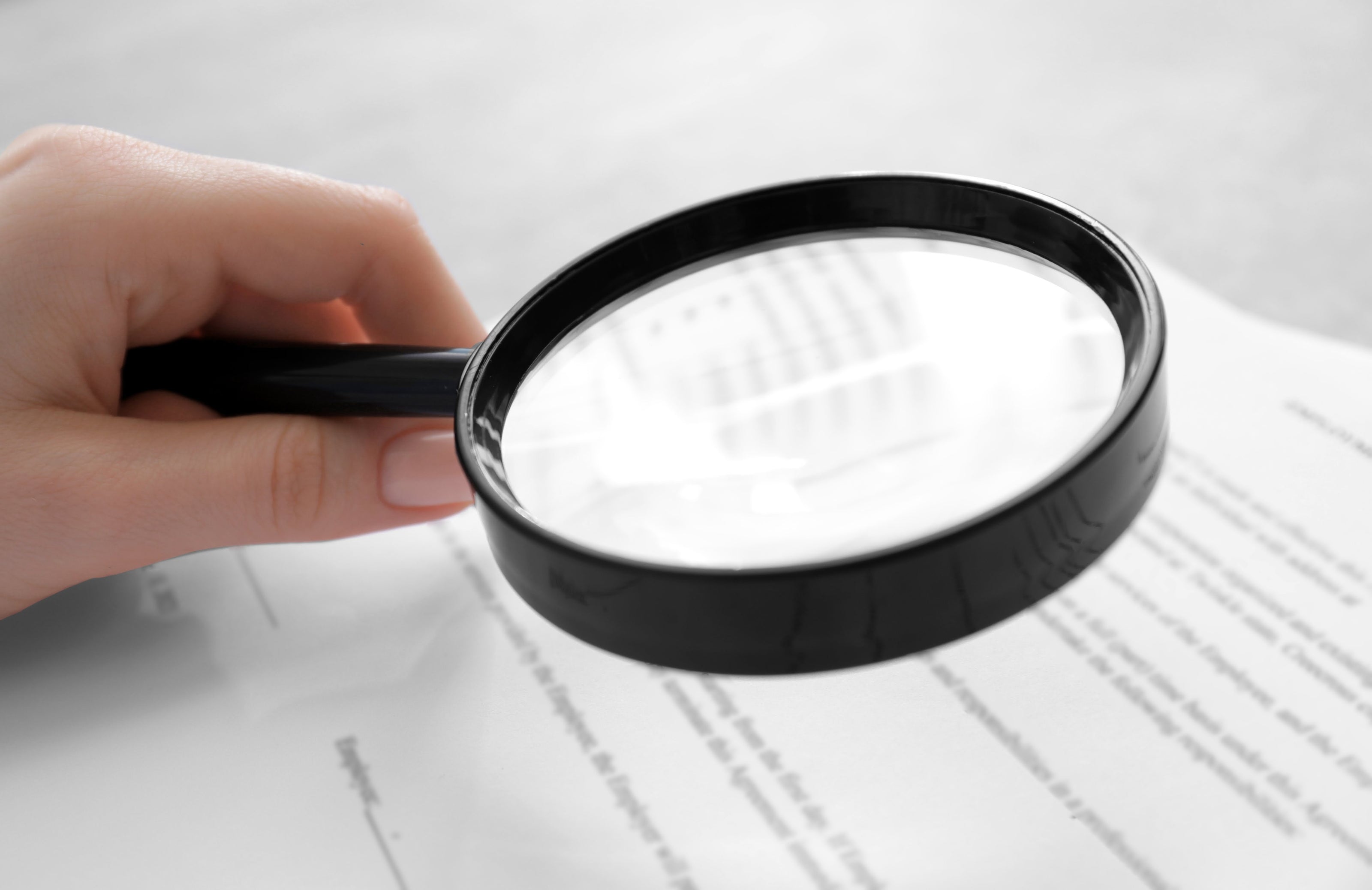 Hand holding a magnifying glass over printed text on a white surface