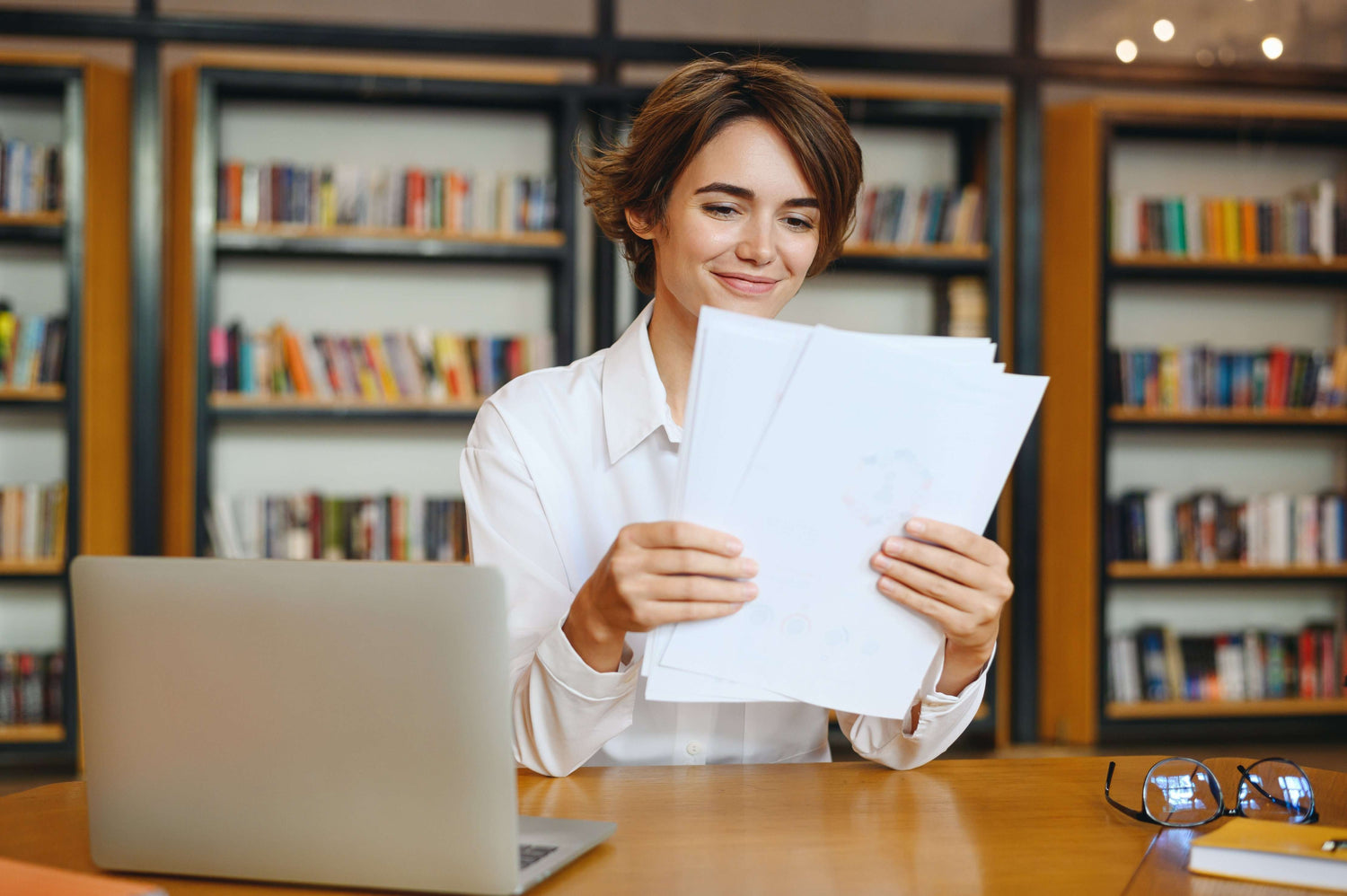 Person holding papers in a library setting with books on shelves in the background