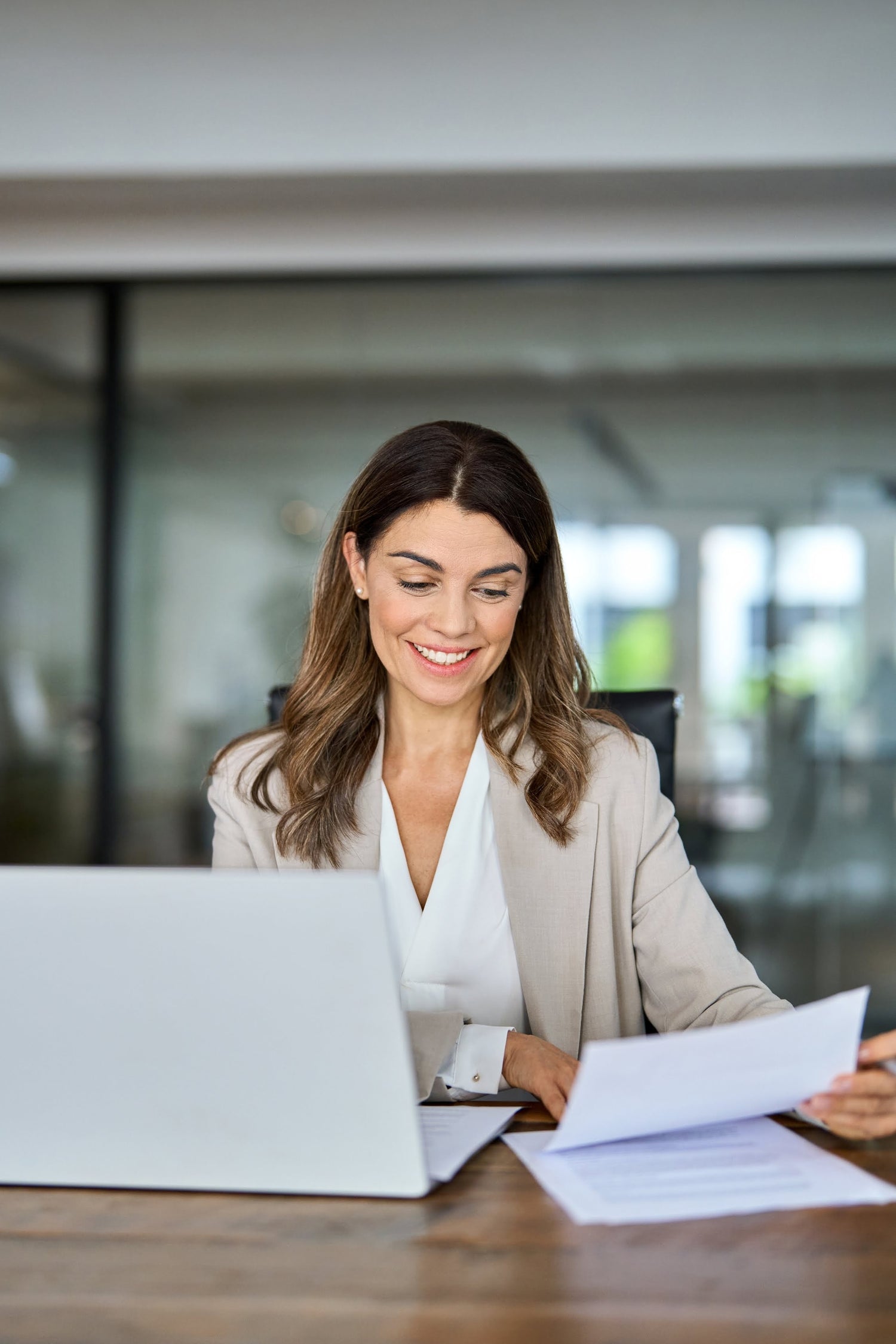 Woman sitting at a desk with a laptop and documents, smiling.