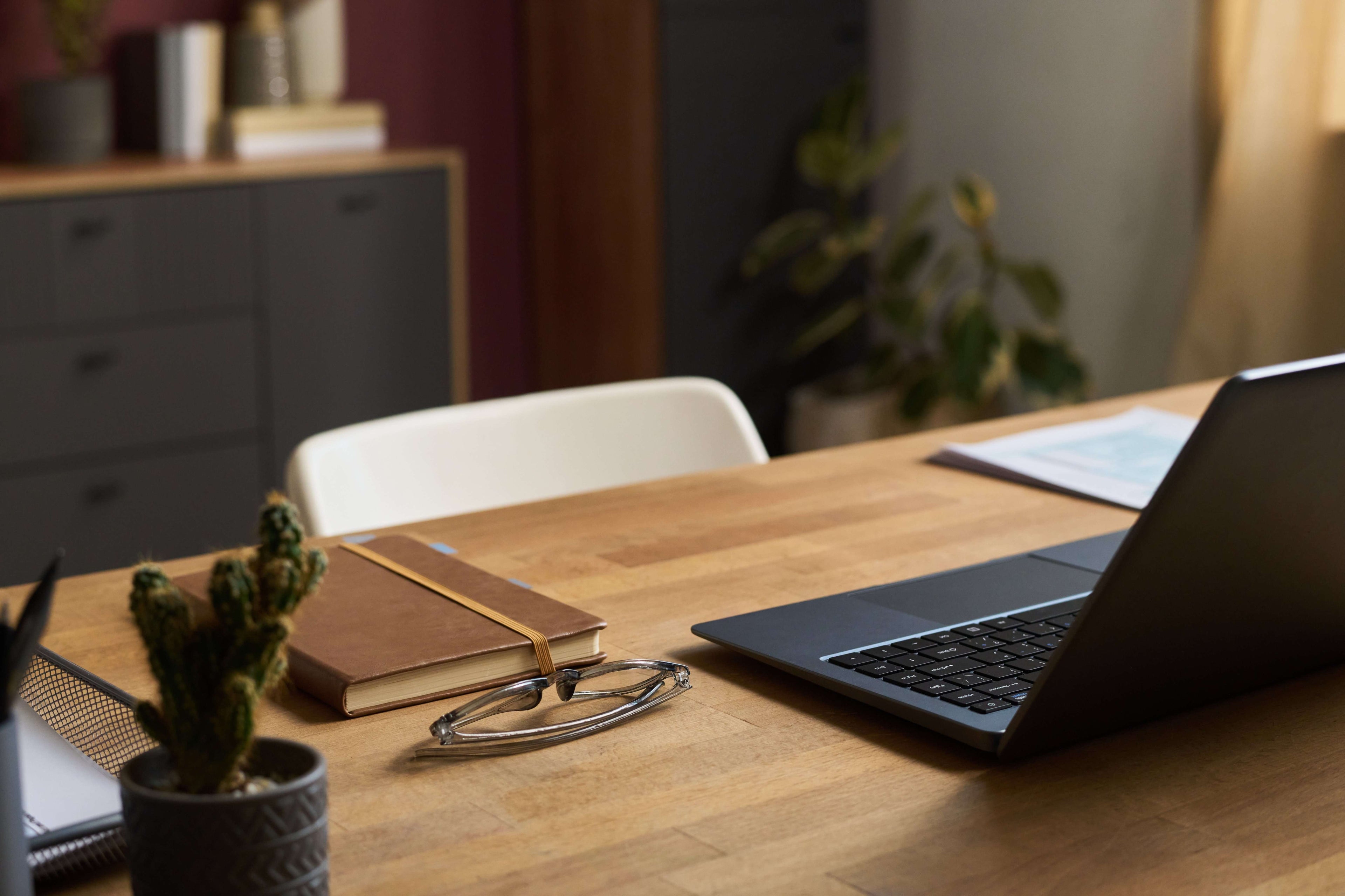 Laptop on a wooden desk with a notebook, plant, and stethoscope in a home office setting.
