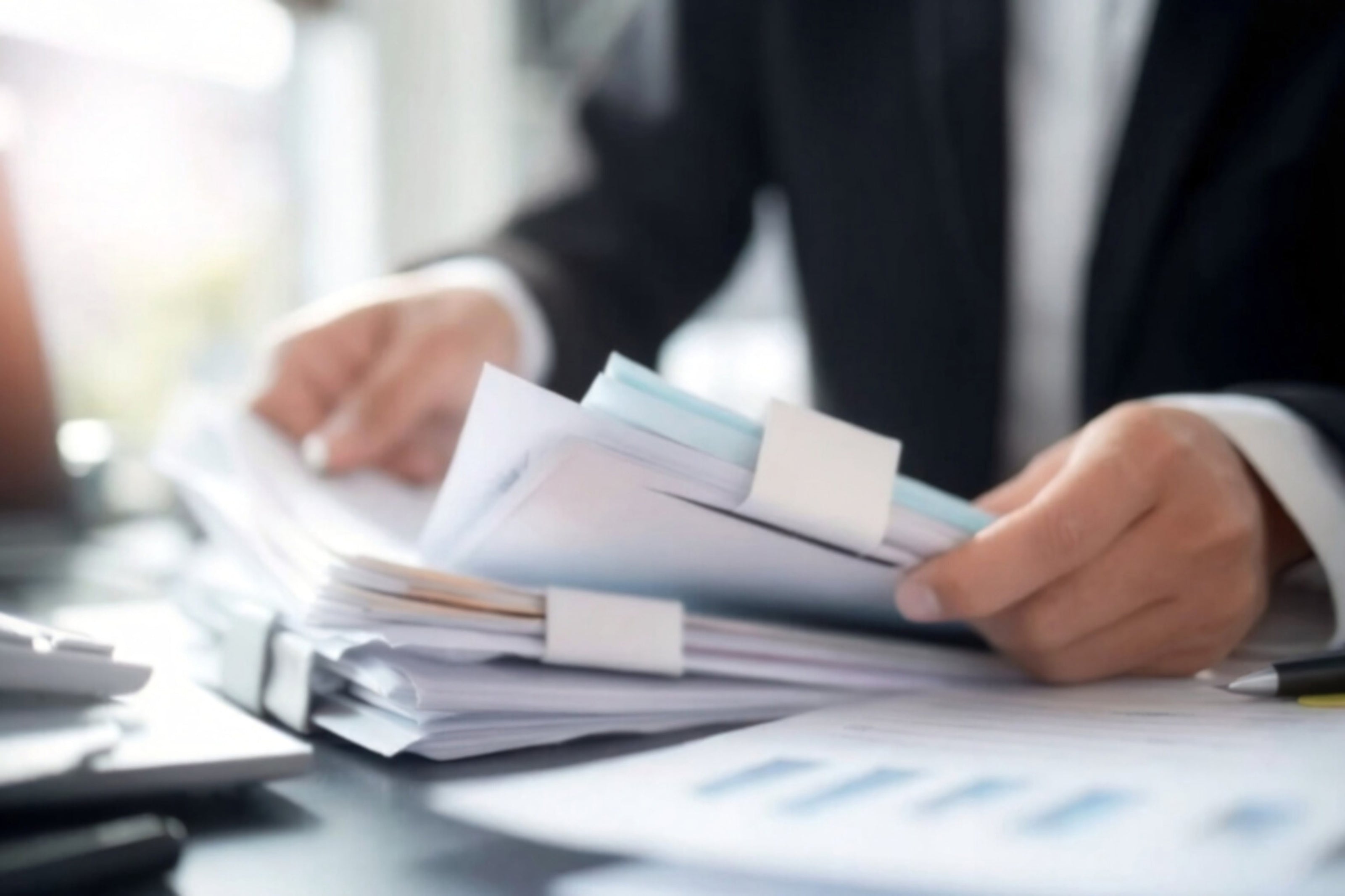 Person holding a stack of papers at a desk