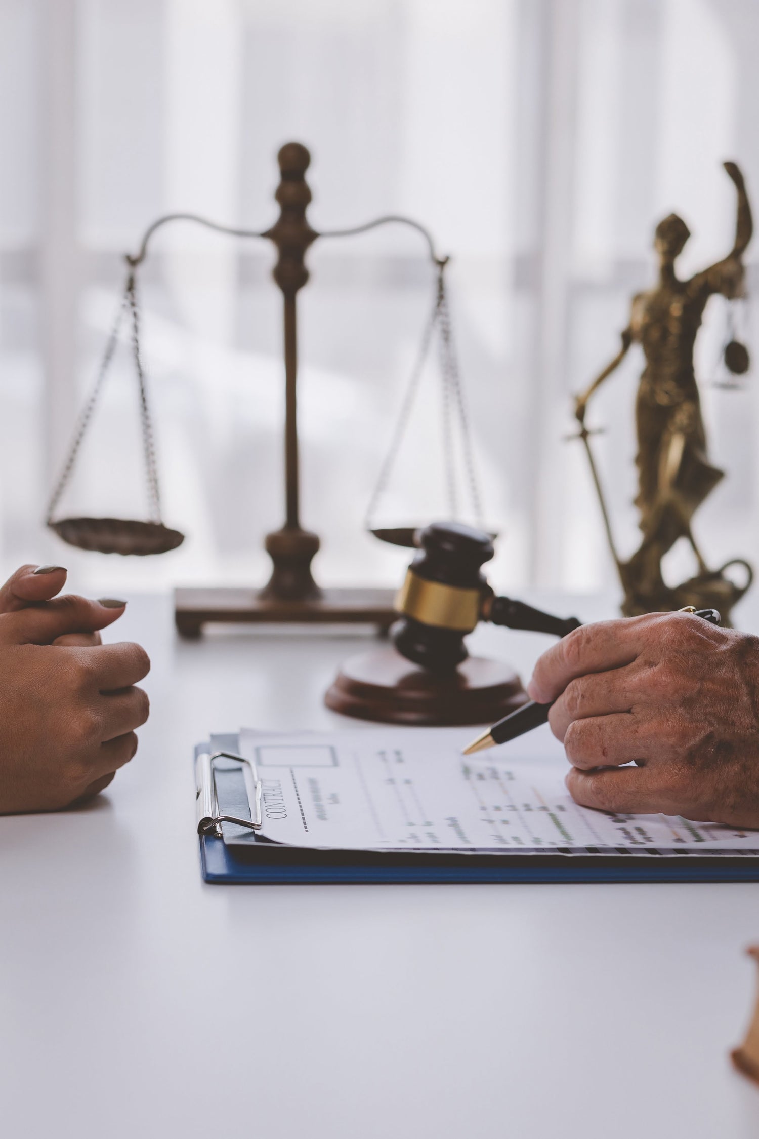 Two people sitting at a table with legal documents, a gavel, and a statue of Lady Justice in the background.