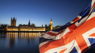 British flag in front of the Houses of Parliament at night.