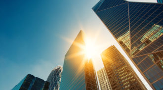 Modern skyscrapers with sunlight reflecting off glass windows against a blue sky.